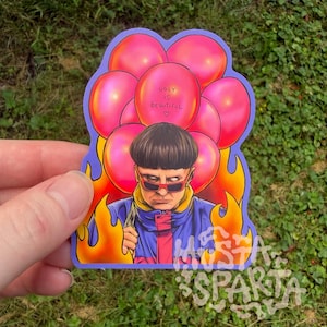 May include: A die-cut sticker featuring a person with a bowl cut wearing red-tinted sunglasses and a blue and yellow jacket. The person is surrounded by bright pink balloons and orange flames. One balloon has the text "ugly is beautiful" written on it.
