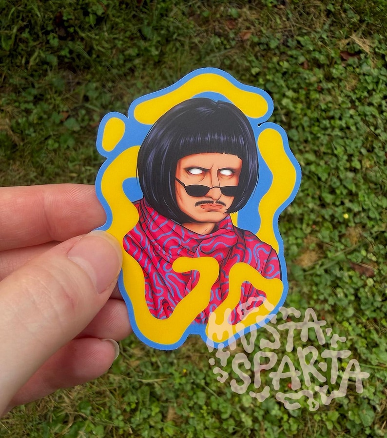May include: A die-cut sticker featuring a character with a black bob haircut, a thin moustache, and white glowing eyes wearing dark sunglasses. The character wears a red and blue patterned scarf against a blue background with yellow organic shapes.