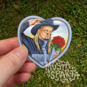 May include: A heart-shaped sticker featuring an illustration of a person with long blonde hair, a mullet, and a goatee, wearing a dark blue cowboy hat and a matching jacket with fringe. The person holds a bouquet of red roses against a yellow sky.