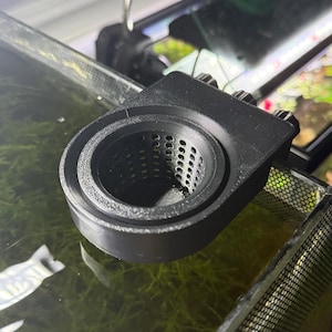 May include: A black, 3D-printed aquarium filter with a cylindrical mesh basket. The filter has a rectangular mounting bracket with three adjustment knobs. The filter is designed to sit inside an aquarium.