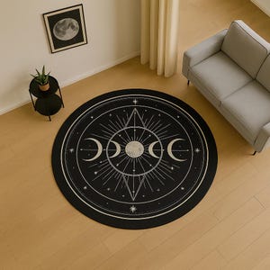 Può includere: Un tappeto rotondo nero con un design celeste bianco con un sole, lune crescenti, stelle e forme geometriche. Il tappeto è posizionato su un pavimento in legno chiaro, con un divano grigio e un piccolo tavolino nero.