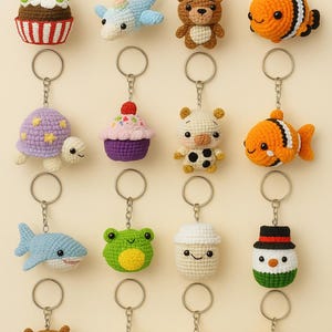 May include: A collection of crochet keychains in various shapes, including a cupcake, dolphin, deer, and fish. Each keychain is attached to a silver ring. The keychains are in various colors, such as blue, orange, and brown.