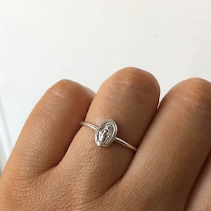 May include: A silver ring with a small oval-shaped charm featuring a depiction of the Virgin Mary.