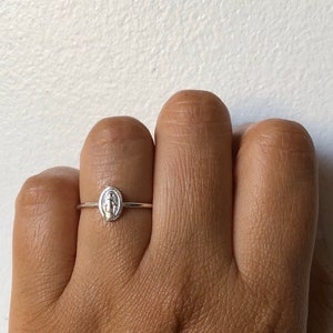 May include: A silver ring with a small oval-shaped charm featuring a depiction of the Virgin Mary.