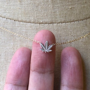 May include: A delicate gold chain necklace with a small silver marijuana leaf pendant.
