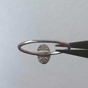 May include: A silver ring with a small oval-shaped stone set in the center. The stone is surrounded by a delicate, textured design.