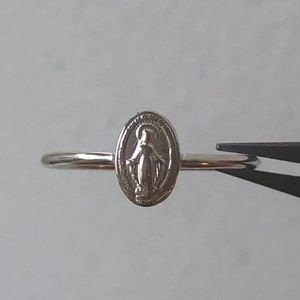 May include: A silver ring with a small oval charm featuring a depiction of the Virgin Mary.