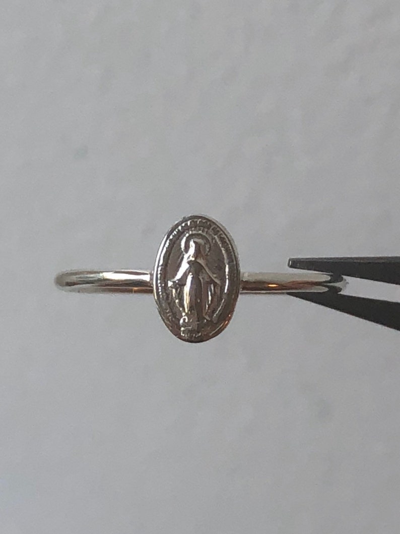 May include: A silver ring with a small oval charm featuring a depiction of the Virgin Mary.