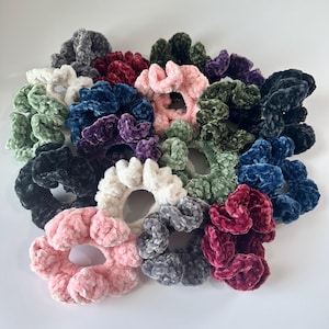 May include: A collection of 15 colorful scrunchies made of soft, fuzzy velvet. The scrunchies are in various colors, including pink, white, green, blue, purple, red, and black.