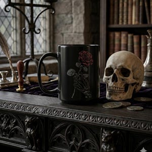 May include: Black ceramic mug with a red rose design held by a skeleton hand. The mug sits on a dark wooden table, alongside a skull and coins. The background includes a candle holder and books, creating a gothic theme.