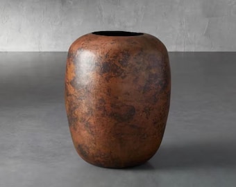 Pode incluir: Um vaso grande, de formato oval, com um acabamento de cobre manchado e texturizado. O vaso tem um corpo largo e uma abertura estreita no topo. A cor é uma mistura de castanho e castanho escuro, com um brilho ligeiramente brilhante. É um adorno decorativo.