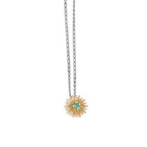 May include: A gold-colored daisy pendant necklace with a small green gemstone center. The pendant is suspended from a silver-colored chain. The necklace is displayed against a white background.