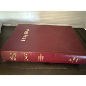 May include: A burgundy-colored Holy Bible with gold lettering. The book is a King James Version (KJV) with the words of Christ in red. The cover is embossed with the title "Holy Bible".