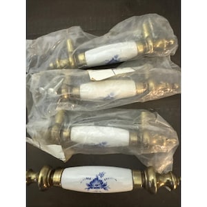 May include: Set of four cabinet pulls. Each pull has a white ceramic center with a blue floral design and brass-colored metal ends. The pulls are packaged in clear plastic.