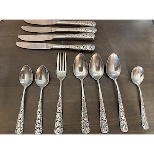May include: A set of silver-colored flatware, including knives, forks, and spoons. The handles feature a detailed leaf design. The set includes six knives, one fork, and seven spoons of varying sizes.