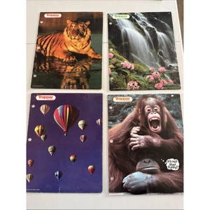 May include: Four Trapper brand notebooks with different cover designs. One features a tiger in water, another a waterfall with pink flowers, a third has hot air balloons, and the last shows an orangutan with the text "It's not that funny!"