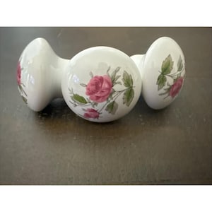 May include: Three white ceramic door knobs with a floral rose design. The roses are pink with green leaves. The knobs are round with a curved base.