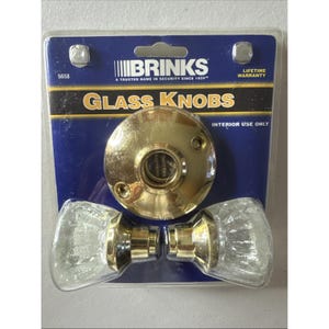 May include: A package of Brinks glass knobs for interior use. The package includes two clear glass knobs with a gold-colored base and a gold-colored circular plate. The package has the text "GLASS KNOBS" and "LIFETIME WARRANTY".