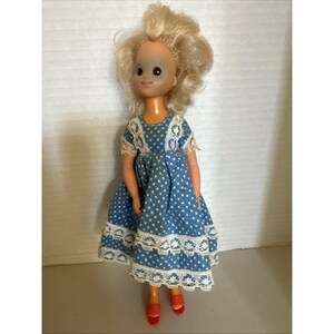 May include: A vintage doll with blonde hair and a blue polka dot dress with white lace trim. The doll has red shoes and is standing upright. The doll's face has painted features.