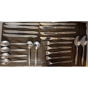 May include: A set of vintage silverware, including knives, forks, and spoons, arranged in a box. The silverware has a floral design on the handles and a shiny, metallic finish. The set includes soup spoons, dinner forks, and butter knives.