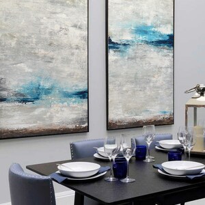 Puede incluir: Dos pinturas abstractas con un esquema de color azul y gris cuelgan de una pared sobre una mesa de comedor negra con cuatro sillas. Las pinturas est&aacute;n enmarcadas en negro.