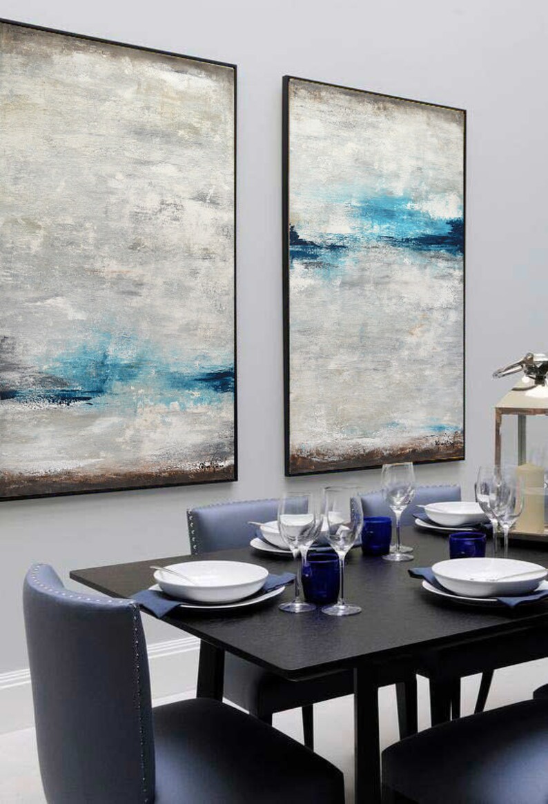 Puede incluir: Dos pinturas abstractas con un esquema de color azul y gris cuelgan de una pared sobre una mesa de comedor negra con cuatro sillas. Las pinturas est&aacute;n enmarcadas en negro.