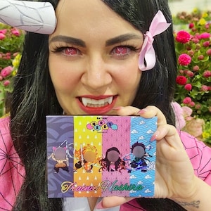 May include: A person holding a colorful eyeshadow palette with the text "Trainee Hashira". The palette features illustrations of anime characters. The palette has a pink, blue, yellow, and purple design.
