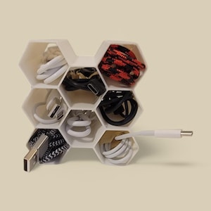 Puede incluir: Organizador de cables hexagonal blanco con múltiples compartimentos llenos de cables de diferentes colores.