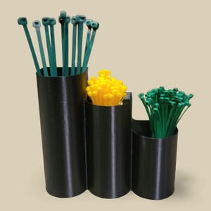 Puede incluir: Un organizador de plástico negro con tres compartimentos, cada uno con bridas de diferentes colores. Los compartimentos contienen bridas verdes, amarillas y más verdes. El organizador está sobre un fondo neutro.