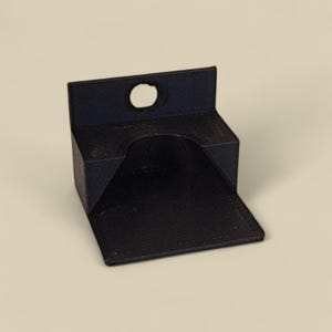 May include: A black plastic wall mount with a small hole in the top and a larger opening at the front. The mount is designed to hold a small object, such as a phone or a tablet.