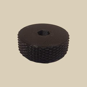 Könnte beinhalten: Dunkelbraunes, kreisförmiges Objekt mit strukturierter, geriffelter Seite und sechseckigem Loch in der Mitte. Die Oberseite ist flach und glatt. Das Objekt scheint aus einem festen Material zu bestehen.