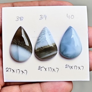 May include: Three pear-shaped cabochon gemstones arranged on a white card. The first, labeled 38, is brown and white with a measurement of 27x17x7 inches. The second, labeled 39, is blue and brown with a measurement of 25x17x7 inches. The third, labeled 40, is solid blue with a measurement of 24x17x7 inches.