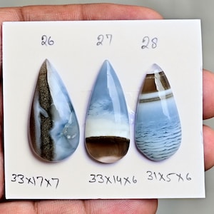 May include: Three teardrop-shaped polished gemstones labeled 26, 27, and 28. Gemstone 26 is brown and blue with a metallic band, measuring 33x17x7 mm. Gemstone 27 is blue and white with a brown base, measuring 33x14x6 mm. Gemstone 28 is blue and brown, 31x5x6 mm.