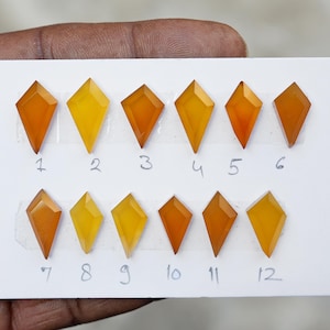 Könnte beinhalten: Zwölf rautenförmige Edelsteine in Orange- und Gelbtönen sind auf einer weißen Oberfläche angeordnet. Jeder Edelstein ist von 1 bis 12 nummeriert. Die Edelsteine variieren in der Farbintensität.