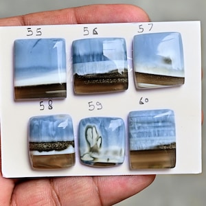 May include: Six rectangular polished gemstones arranged on a white card, labeled 55 through 60. Each stone features horizontal bands of light blue, white, and translucent brown, with some showing metallic-looking inclusions within the layers.