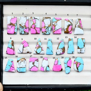 May include: A collection of twenty-one polished gemstones in various shapes, including rectangles, triangles, and ovals. The stones feature a mix of colors: pink, white, turquoise, and brown. Each stone is unique, with a marbled or patterned appearance.