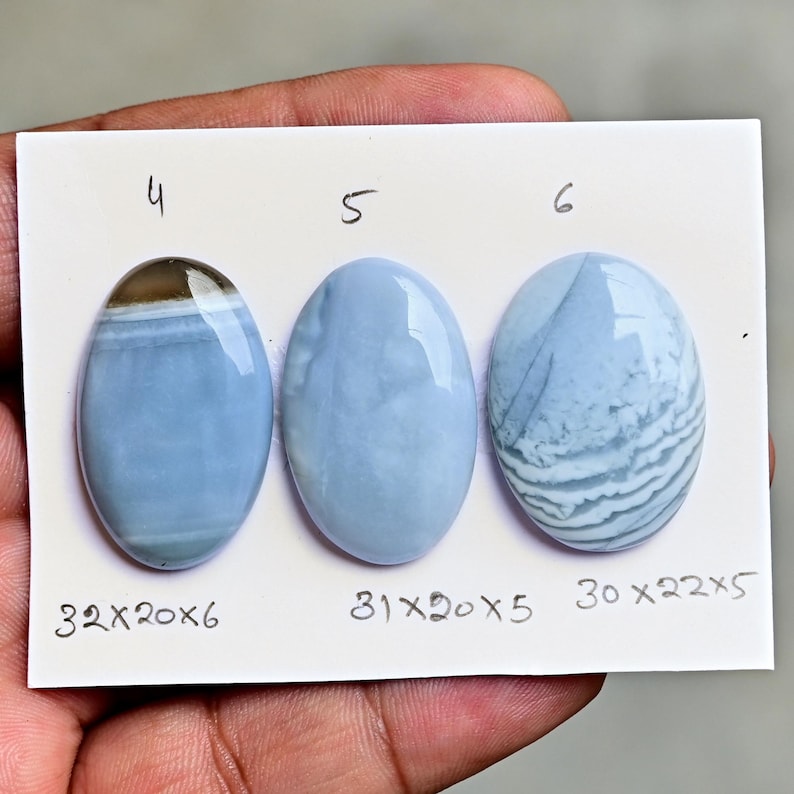 May include: Three oval-shaped blue gemstones labeled 4, 5, and 6 on a white card. Gemstone 4 measures 32x20x6 mm, gemstone 5 measures 31x20x5 mm, and gemstone 6 measures 30x22x5 mm. Each stone features smooth, polished surfaces with unique patterns.