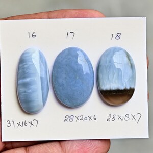 May include: Three oval-shaped blue gemstones labeled 16, 17, and 18 on a white card. Gemstone 16 measures 31x16x7 mm, gemstone 17 measures 28x20x6 mm, and gemstone 18 measures 28x18x7 mm, featuring a distinct brown band at the base.