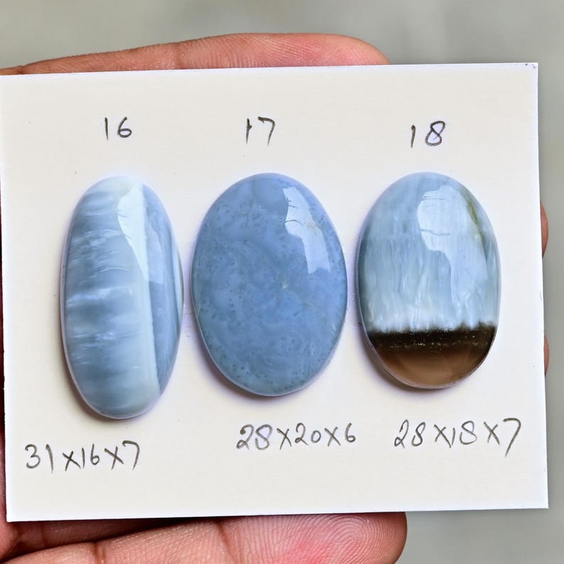 May include: Three oval-shaped blue gemstones labeled 16, 17, and 18 on a white card. Gemstone 16 measures 31x16x7 mm, gemstone 17 measures 28x20x6 mm, and gemstone 18 measures 28x18x7 mm, featuring a distinct brown band at the base.