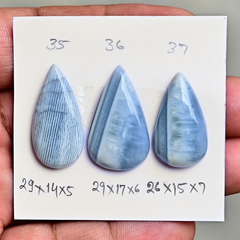 May include: Three pear-shaped blue and white cabochons arranged on a white card. The stones are labeled 35, 36, and 37 with dimensions 29x14x5, 29x17x6, and 26x15x7 written in black ink below each corresponding stone on the white card.