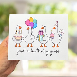 May include: A white greeting card featuring four cartoon geese celebrating. One holds a cake with candles, one holds colorful balloons, one holds stacked gift boxes, and one wears a party hat with a cupcake and confetti. Text reads: just a birthday goose.