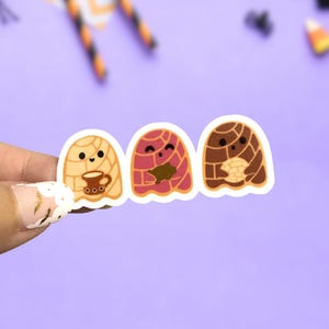 May include: Three stickers featuring cartoon versions of concha bread, each with a unique design. One holds a coffee cup, another has a filling, and the third has a bite taken out. The stickers are on a purple background with Halloween-themed decorations.