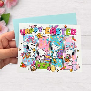 May include: Easter greeting card featuring Snoopy characters with bunny ears, holding Easter eggs and baskets. The card has the words "Happy Easter" in colorful letters. The card is held in front of a light blue envelope.