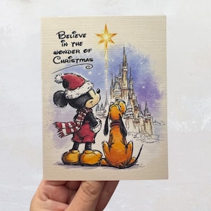 May include: A Christmas card featuring Mickey Mouse and Pluto looking at a star and a castle. The card has the text "Believe in the Wonder of Christmas" in black script. Mickey Mouse wears a Santa hat, red coat, and scarf.