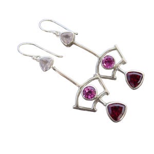 May include: Silver dangle earrings with pink and red gemstones. The earrings feature a geometric design with a fan-shaped element.