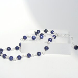 May include: A silver chain necklace with dark blue lapis lazuli beads. The necklace is on a white surface.