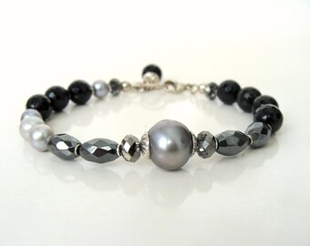 May include: A silver bracelet with black, gray, and white beads. The bracelet has a large gray pearl in the center.