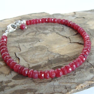 May include: A red gemstone bracelet with a silver clasp. The bracelet is made of small, faceted beads and is strung on a silver chain.