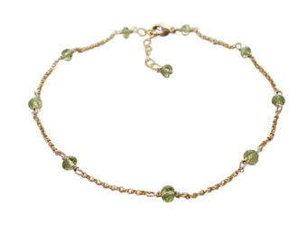 May include: A gold chain anklet with small green gemstone beads.