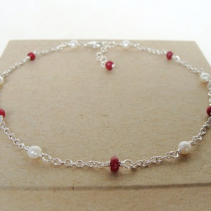 May include: A silver chain anklet with alternating red and white beads.